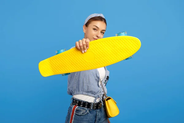 Foto av vacker ung kvinna hålla gul öre eller skateboard framför ansiktet över Blå bakgrund. — Stockfoto