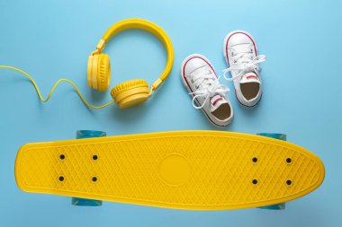 Sarı kulaklıklar, beyaz spor ayakkabılar ve kaykay ya da mavi arka plan üzerinde pennyboard. Müzik konsepti.