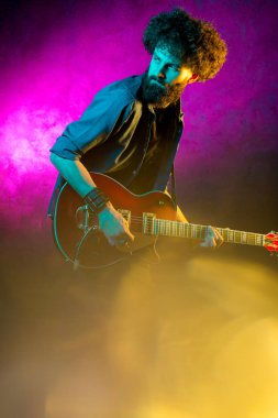 Neon ışıklar kırmızı gitar ile kıvırcık saçlı genç hipster adam. Rock müzisyeni elektrik gitar çalıyor.