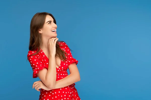 Vonzó fiatal nő, világos mosoly piros ruhában látszó el több mint kék háttér. — Stock Fotó