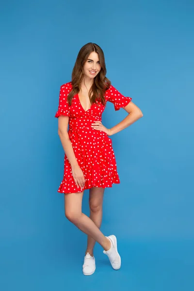 Foto de cuerpo entero de mujer joven con sonrisa brillante en vestido rojo posando a la cámara sobre fondo azul . — Foto de Stock