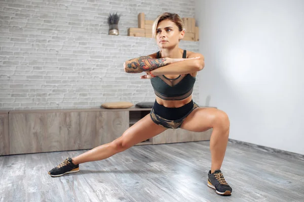 Atractiva rubia joven delgada mujer en ropa deportiva que se extiende en el gimnasio. Mujer haciendo ejercicio de estiramiento warmup . —  Fotos de Stock