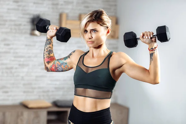 Spor salonunda omuzlar için ağır halter egzersiz yapıyor Atletik genç sarışın kadın.