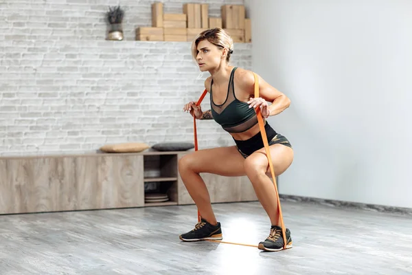 Çekici sporcu genç sarışın kadın spor salonunda bantlarla egzersiz yapıyor..