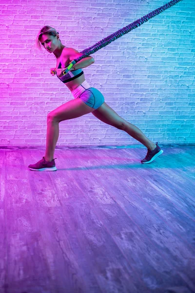 Attractive desportivo jovem loira treino com bandas elásticas no ginásio em luzes de néon . — Fotografia de Stock