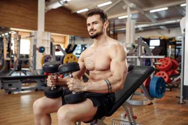 Spor salonundaki dambılla egzersiz yapmaya odaklanan kaslı sporcu vücut geliştirme fitness modeli..