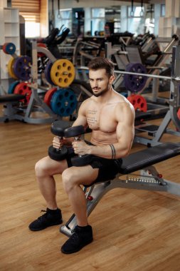 Spor salonundaki dambılla egzersiz yapmaya odaklanan kaslı sporcu vücut geliştirme fitness modeli..