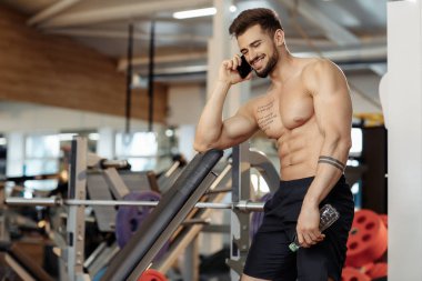 Spor salonunda akıllı telefon veya cep telefonu çekici atletik genç adam vücut geliştirmeci fitness modeli konuşmak.