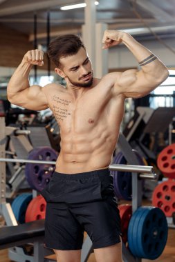 Kas atletik genç adam vücut geliştirmeci fitness modeli spor salonunda egzersizleri sonra onun pazı göstermek.