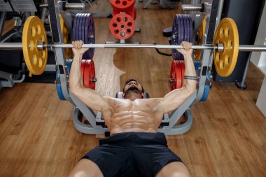 Spor salonunda bankta halter ile güçlü atletik genç adam vücut geliştirmeci fitness modeli egzersiz göğüs. Üstte görüntü.