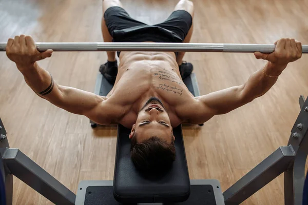 Fuerte atlético joven culturista modelo fitness pecho de ejercicio con barra de pesas en el banco en el gimnasio. Vista superior . —  Fotos de Stock