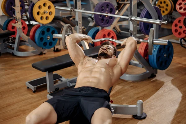 强壮的运动青年男子健美健身模型锻炼三头肌与杠铃在健身房的长凳上. — 图库照片