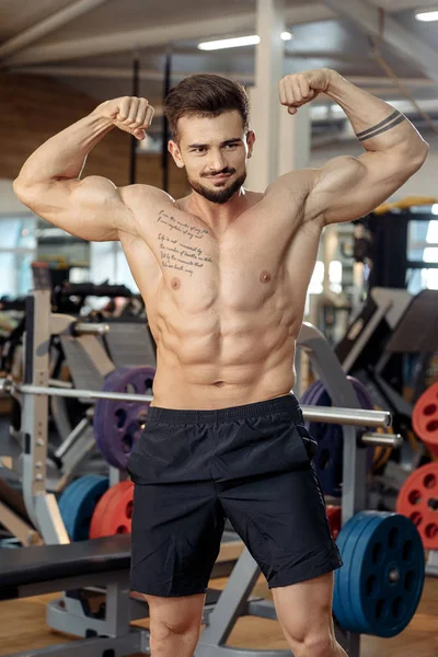 英俊的肌肉运动年轻男子健美健身模型显示他的二头肌后，在健身房锻炼. — 图库照片