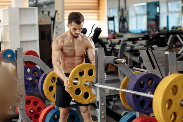 Sterk, atletisk, ung mannskropp-modell, som legger vekt på barbell på benken i gymsalen. – stockfoto