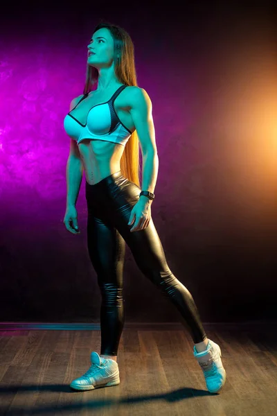 Full lenght photo of beautiful young woman fitness model posing in neon lights in the studio. — Stock Photo, Image
