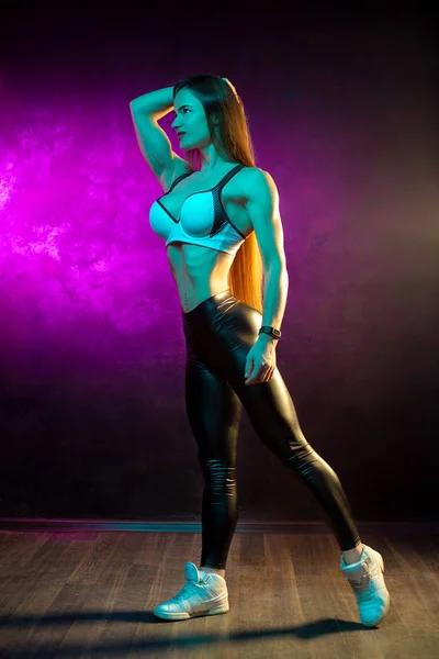 Full lenght photo of beautiful young woman fitness model posing in neon lights in the studio. — Stock Photo, Image