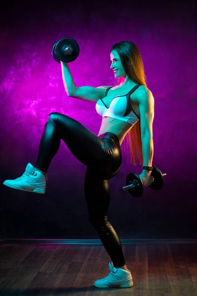 Entraînement motivé de modèle de fitness jeune femme avec haltères professionnelles dans les néons en studio . — Photo