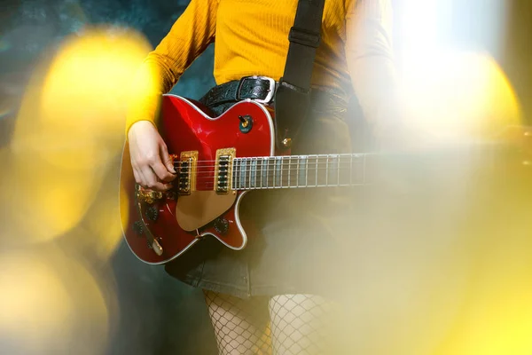 Närbild foto av unga hipster kvinna ben och röd gitarr i neonljus. Rock musiker spelar elgitarr. 90-talets stil koncept. — Stockfoto