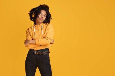 Sarı arka plan üzerinden müzik dinleyen akıllı telefon ve kulaklık ile rahat giysiler giymiş ciddi yüzü ile çekici Afrikalı-Amerikalı genç kadın.
