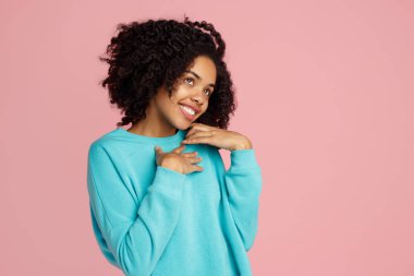 Mutlu Afro-Amerikan genç kadın pembe arka planda poz veriyor..