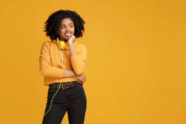 Allvarlig afrikansk amerikansk ung kvinna klädd i casual kläder och hörlurar tittar bort över gul bakgrund. — Stockfoto