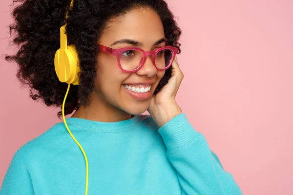 Afryki amerykański, piękna, młoda kobieta z uśmiechem jasne ubrani w ubranie, okulary i słuchawki na różowym tle. — Zdjęcie stockowe