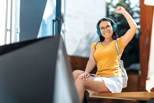 Gelukkig brunette jonge vrouw met heldere glimlach gekleed in Casual kleding luisteren naar muziek met een koptelefoon en glimlachend. — Stockfoto