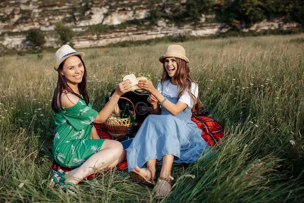 Δύο ελκυστικές κοπέλες κάθονται κάτω στην κουβέρτα πικ-νικ και να διασκεδάσουν. Μπίρας και σάντουιτς. — Φωτογραφία Αρχείου