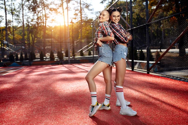 Dua gadis muda hipster cantik berpose dengan wajah bahagia di stadion. Konsep Kebebasan dan Sahabat . — Stok Foto