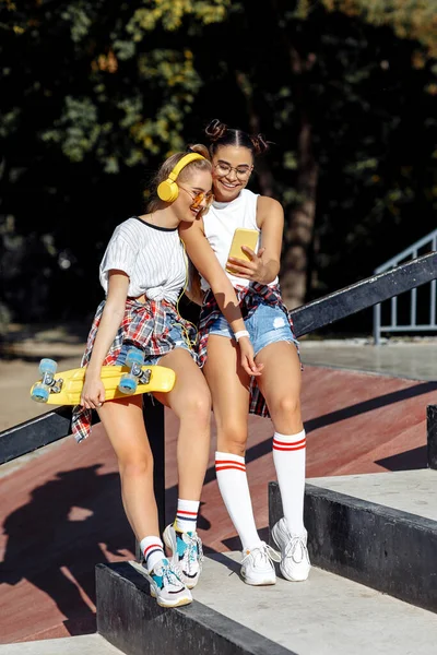 İki genç kızın tam boy görüntüsü kaykay parkında akıllı telefon kullanıyor. Özgürlük ve En İyi Arkadaş kavramı. — Stok fotoğraf