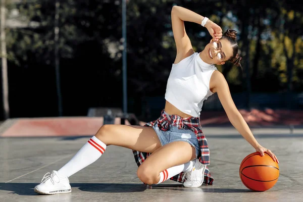 Unachtsame brünette junge Frau posiert mit Basketballkorb im Skatepark. — Stockfoto