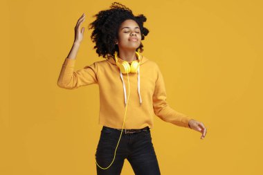 Sarı arka planda dans eden, gündelik giysiler giymiş güzel Afro-Amerikan genç bayan..