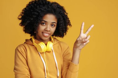 Sarı arka planda barış jesti gösteren gündelik kıyafetler giymiş güzel Afrikalı Amerikalı genç bir kadın..