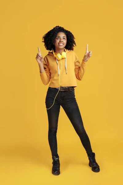 Beautiful african american young woman dressed in casual clothes clothing pointing fingers up over yellow background.