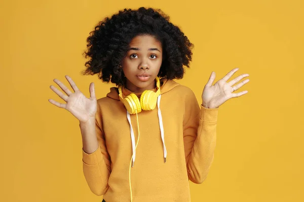 Verblüffte afrikanisch-amerikanische junge Frau in lässiger Kleidung und Kopfhörer über gelbem Hintergrund. — Stockfoto