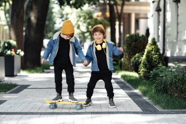 Two adorable twin boys play with skateboard or pennyboard with happy faces in the street.