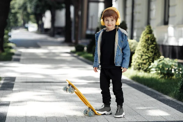 Photo of cute little boy posing with headphones and skateboard in street. — Φωτογραφία Αρχείου