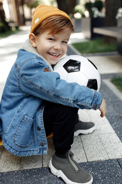 ストリートでサッカーボールでポーズをとるかわいい男の子の写真. — ストック写真