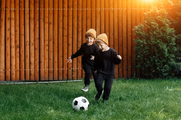 Dos adorables gemelos juegan al fútbol con la pelota clásica en el césped en casa . — Foto de Stock