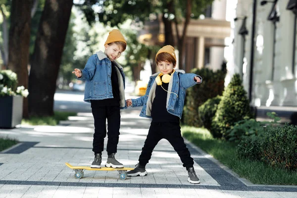 Two gleeful twin boys play with skateboard or pennyboard in the street. — Φωτογραφία Αρχείου