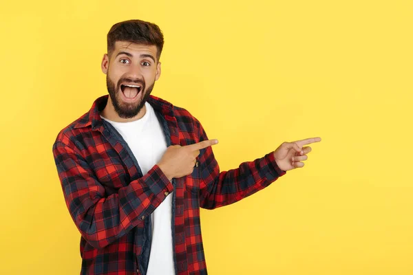 Verrukte bebaarde hipster jongeman in geruite shirt wijzen vingers weg over gele achtergrond. Kijk in de camera.. — Stockfoto