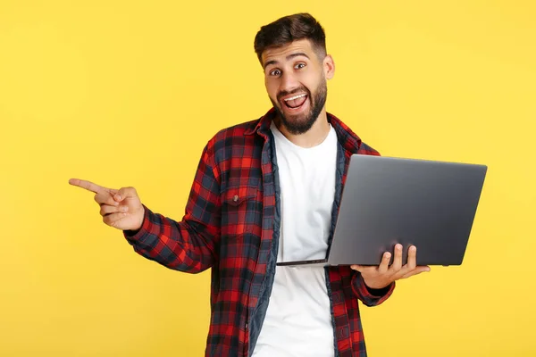 Gelukkig bebaarde hipster jongeman in geruite shirt houden computer wijs vinger weg over gele achtergrond. — Stockfoto