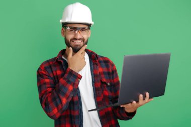 Yeşil arka planda bilgisayarı olan yakışıklı sakallı mühendis ya da müteahhit..