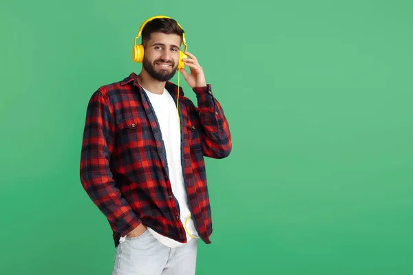 Stijlvolle bebaarde hipster jongeman in geruite shirt met koptelefoon groene achtergrond. — Stockfoto