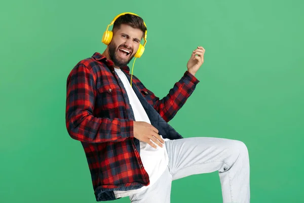 Gioioso giovane hipster barbuto in camicia a quadri che ascolta musica in cuffia e danza su sfondo verde. — Foto Stock