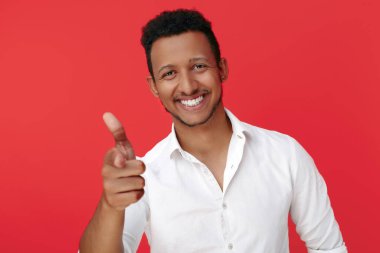 Gülümseyen Afrikalı Amerikalı genç adam kırmızı arka planda kamerayı işaret ediyor..