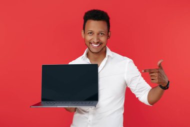 Mutlu Afrikalı Amerikalı genç adam dizüstü bilgisayarını tutuyor ve kırmızı arkaplanı işaret ediyor..