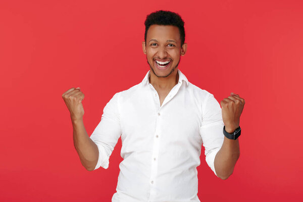 Excited successful african american young man celebrate victory over red background.