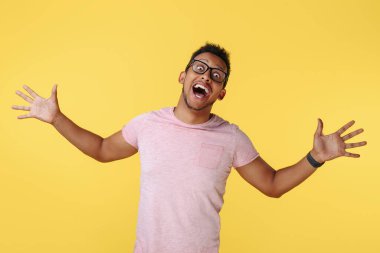 Şaşırmış başarılı Afrikalı Amerikalı genç adam sarı arka planda elleri açık bağırıyor..
