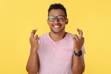 Yakışıklı Afro-Amerikan genci sarı arka planda umut içinde dua ediyor..